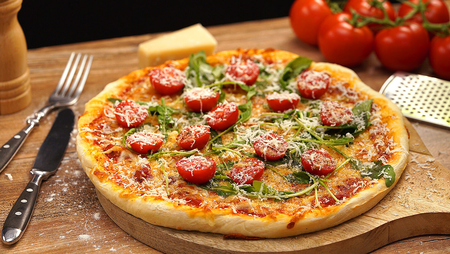 Selbstgemachte Pizza mit Rucola, Tomaten und geriebenem Käse