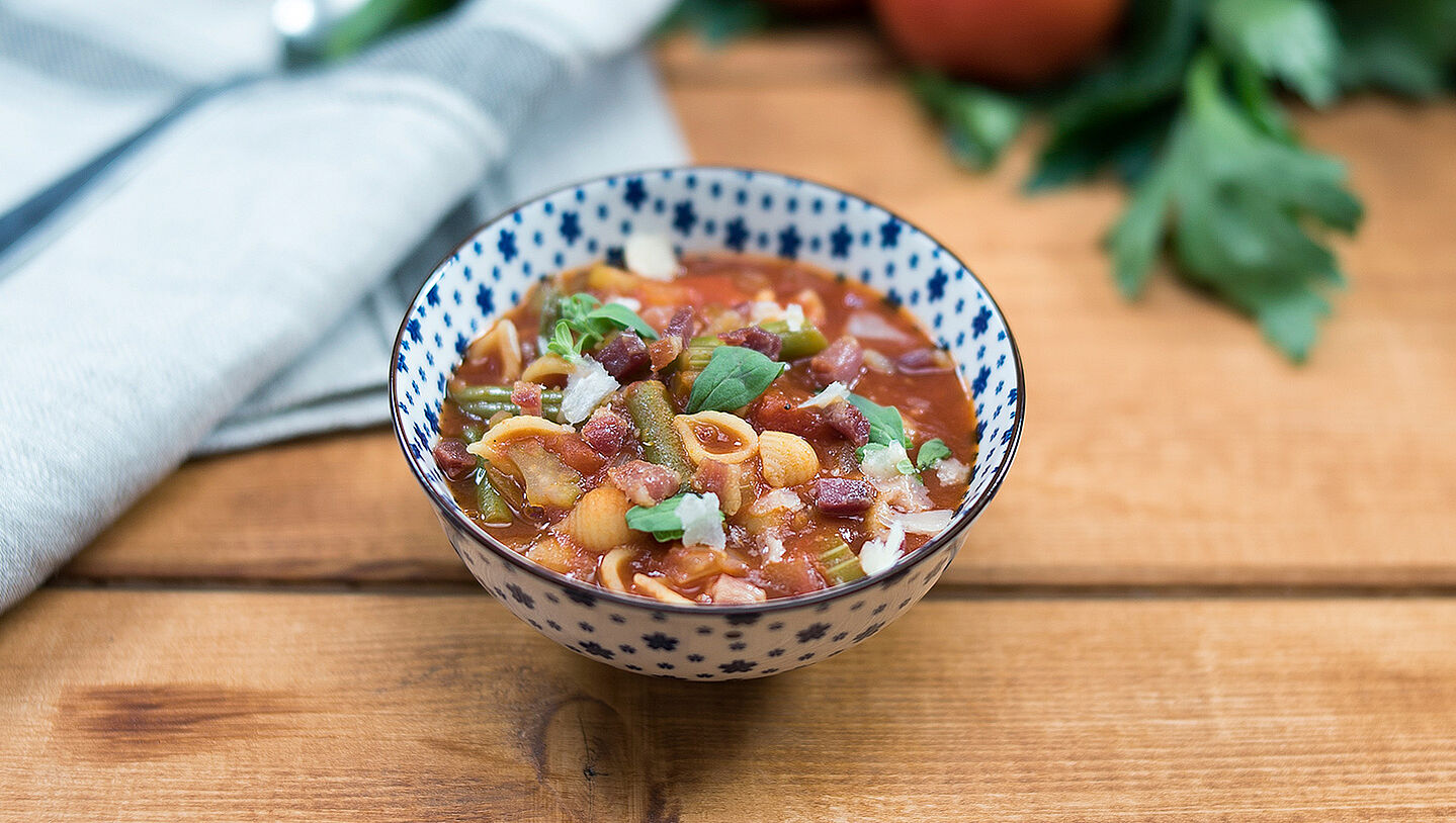 Minestrone in einer blau-weißen Schüssel mit Kräutern dekoriert