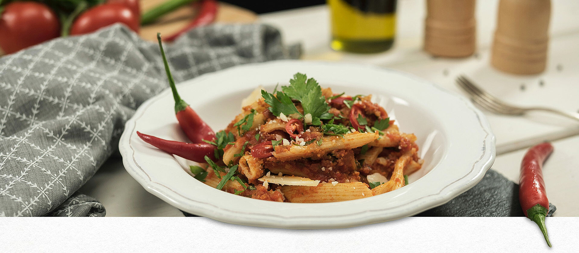 Penne all’arrabbiata auf einem weißen Pastateller mit Petersilie, geriebenem Parmesan und zwei Chilischoten garniert