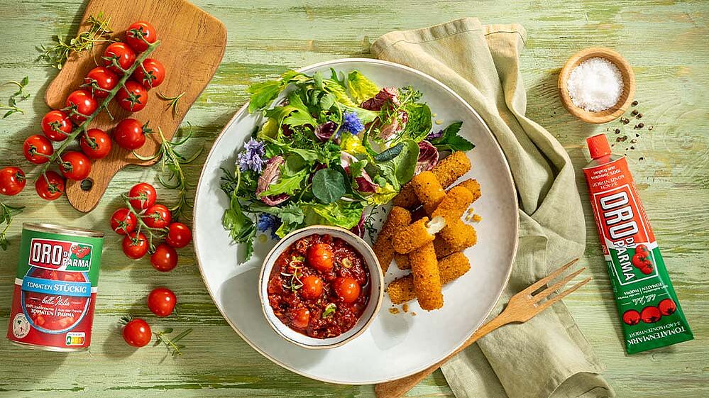 Selbstgemachte Mozzarella-Sticks in einer Schüssel, daneben eine kleinere Schüssel mit Kirschtomaten-Kräuter-Dip