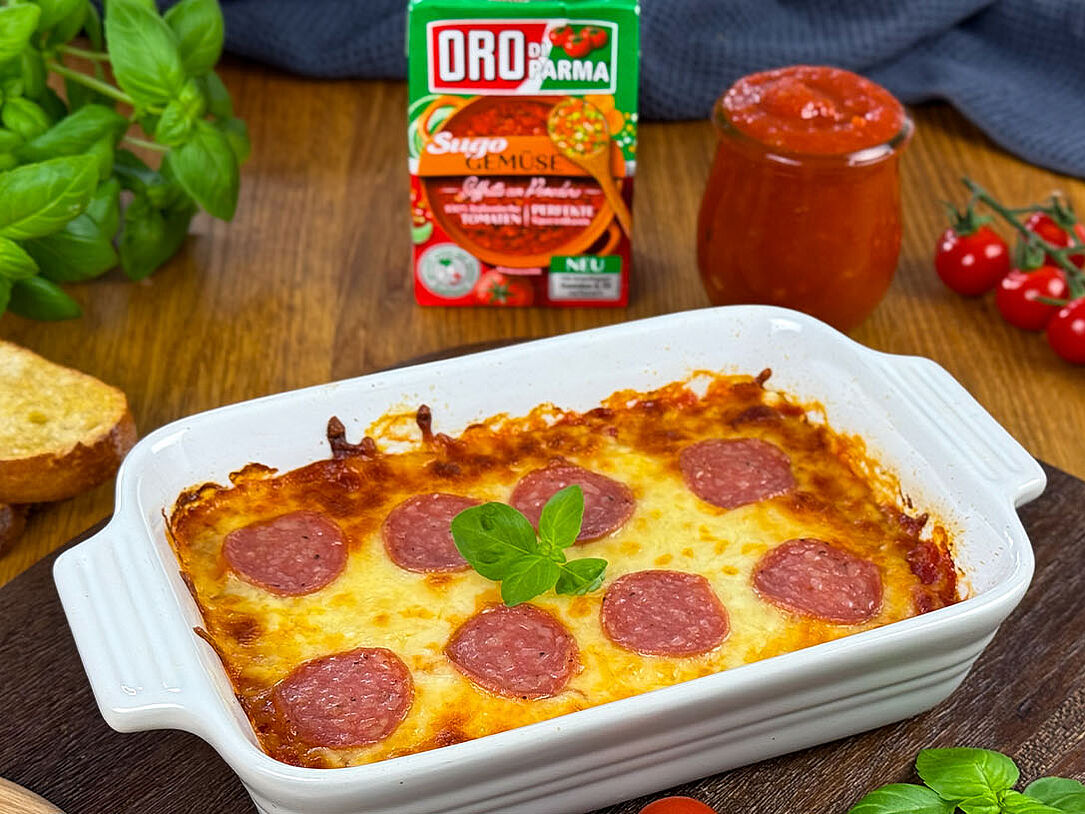 Pizzadip in Auflaufform mit Basilikum auf Holzbrett, dazu geröstetes Ciabatta