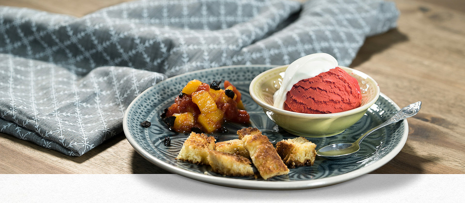 Auf einem Teller liegen gebratene Brioche-Stücke, daneben eine Schüssel mit Tomatensorbet und Tomaten-Mango-Kompott