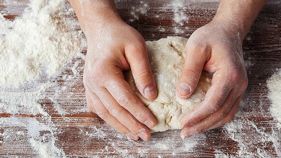 Zwei Hände kneten Pizzateig