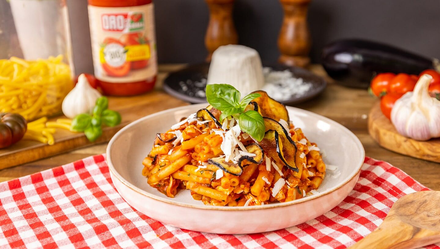 Pasta alla Norma mit Auberginenchips auf einem weißen Teller angerichtet