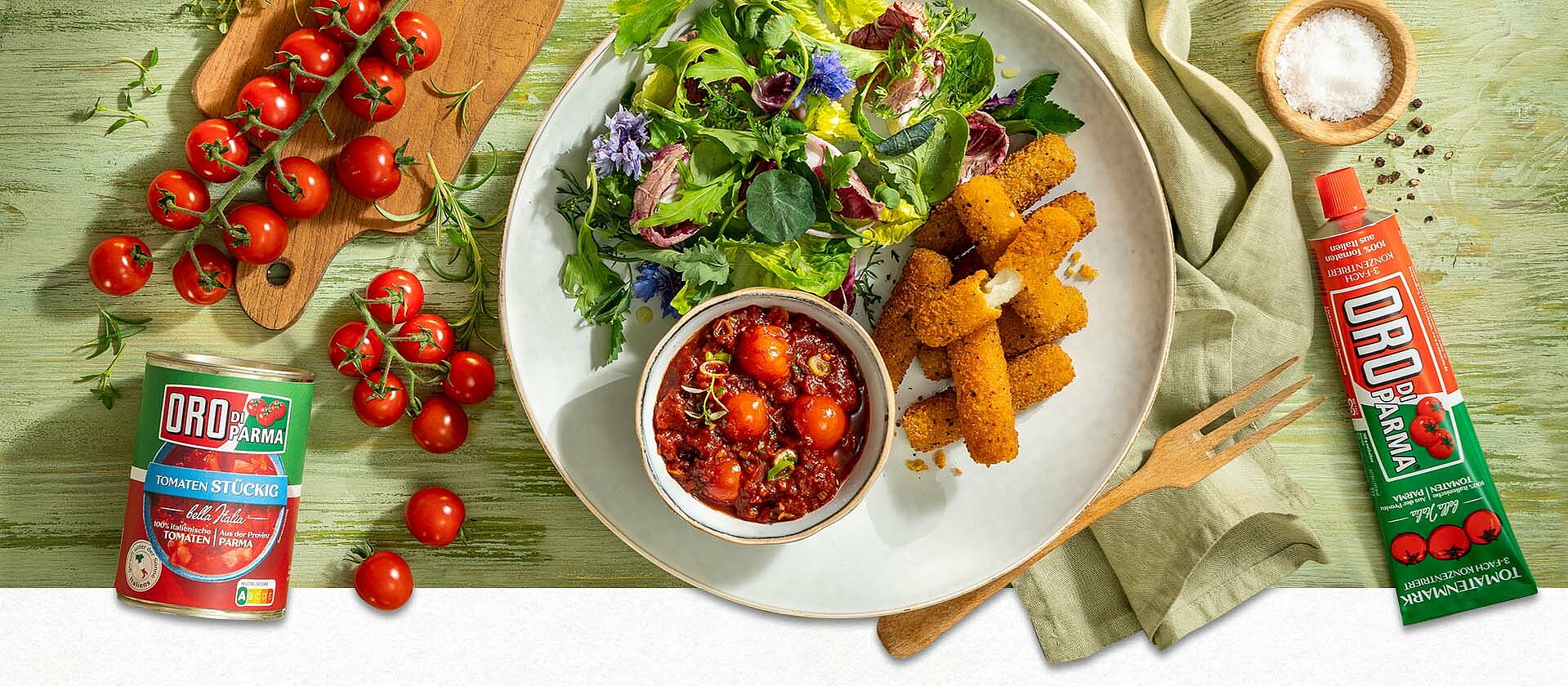 Selbstgemachte Mozzarella-Sticks in einer Schüssel, daneben eine kleinere Schüssel mit Kirschtomaten-Kräuter-Dip