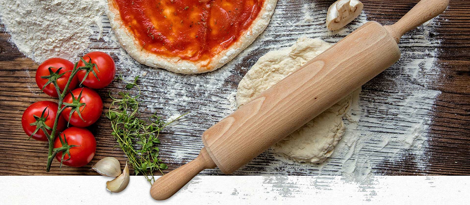 Pizzateig mit Tomatensauce und Zutaten auf Holztisch