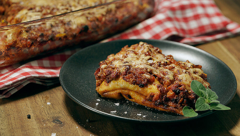 Crespelle - italienische Pfannkuchen gefüllt mit Bolognese auf einem schwarzen Teller