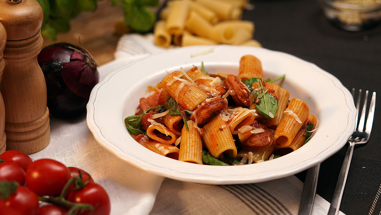 Rigatoni-Nudeln mit Salsiccia-Tomatensauce auf einem weißen Pastateller