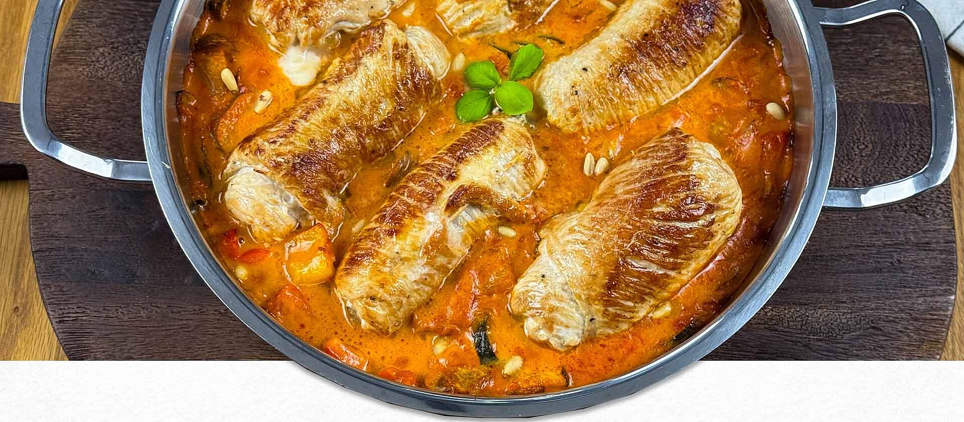 Puten-Involtini mit mediterranem Pfannengemüse in cremiger Soffritto-Sahnesoße – angerichtet im Topf auf einem rustikalem Holzbrett.