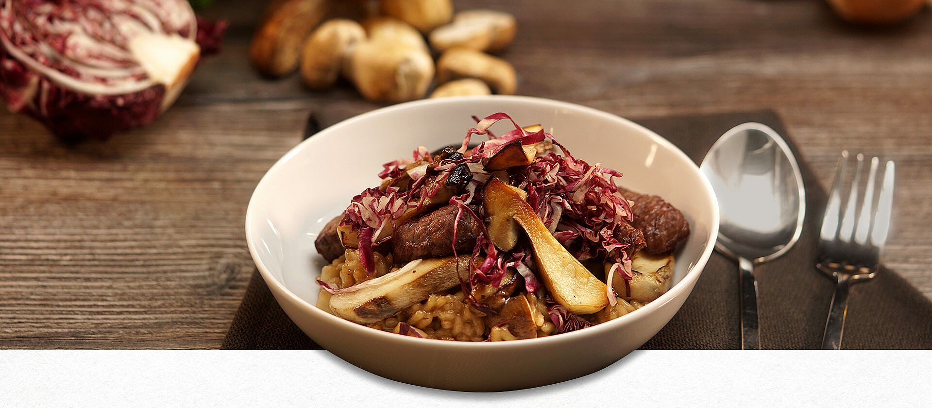 Eine Schüssel gefüllt mit Steinpilzrisotto, rechts daneben ein Löffel und eine Gabel