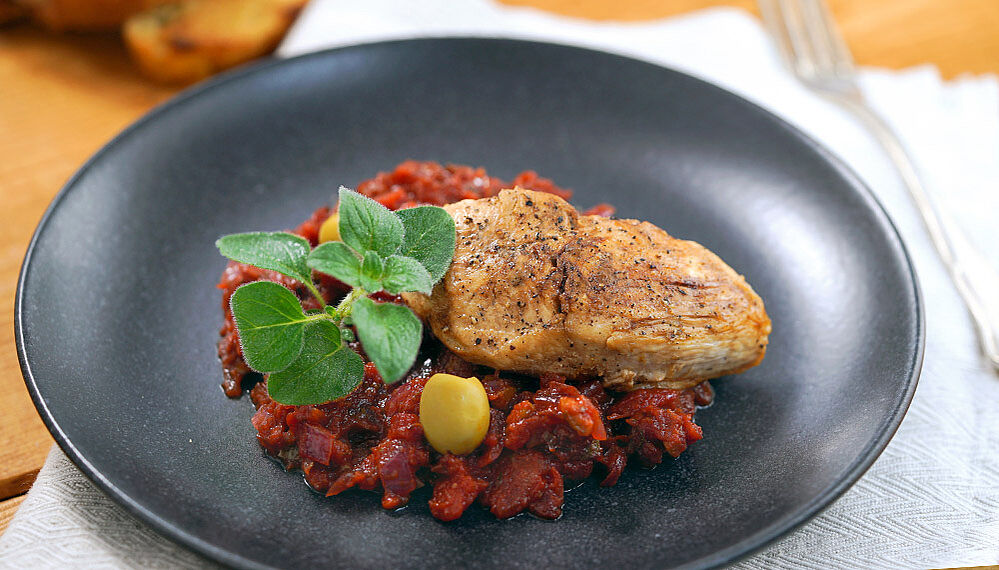 Schwarzer Teller mit Tomaten-Oliven-Sauce und einer Hähnchenbrust.