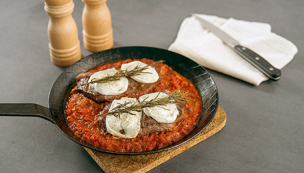 Eiserne Pfanne mit Bistecca con Pomodoro steht auf einem Tisch