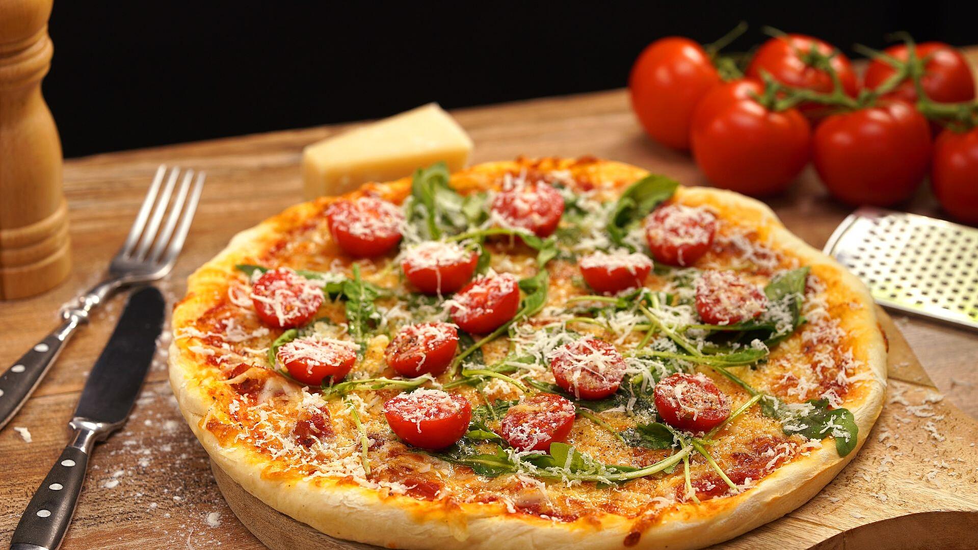 Selbstgemachte Pizza mit Rucola, Tomaten und geriebenem Käse