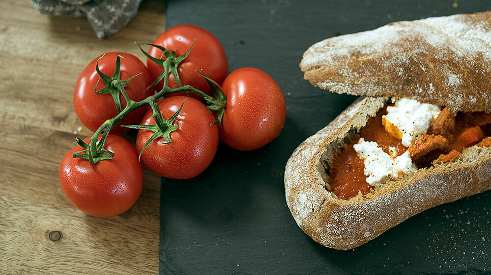 Paprika-Tomatensuppe in einem Ciabatta-Brot serviert, daneben ein Tomatenzweig