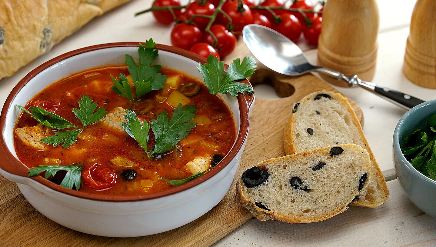 Eine Schüssel mit Tomaten-Fischsuppe, daneben zwei Scheiben Olivenbrot