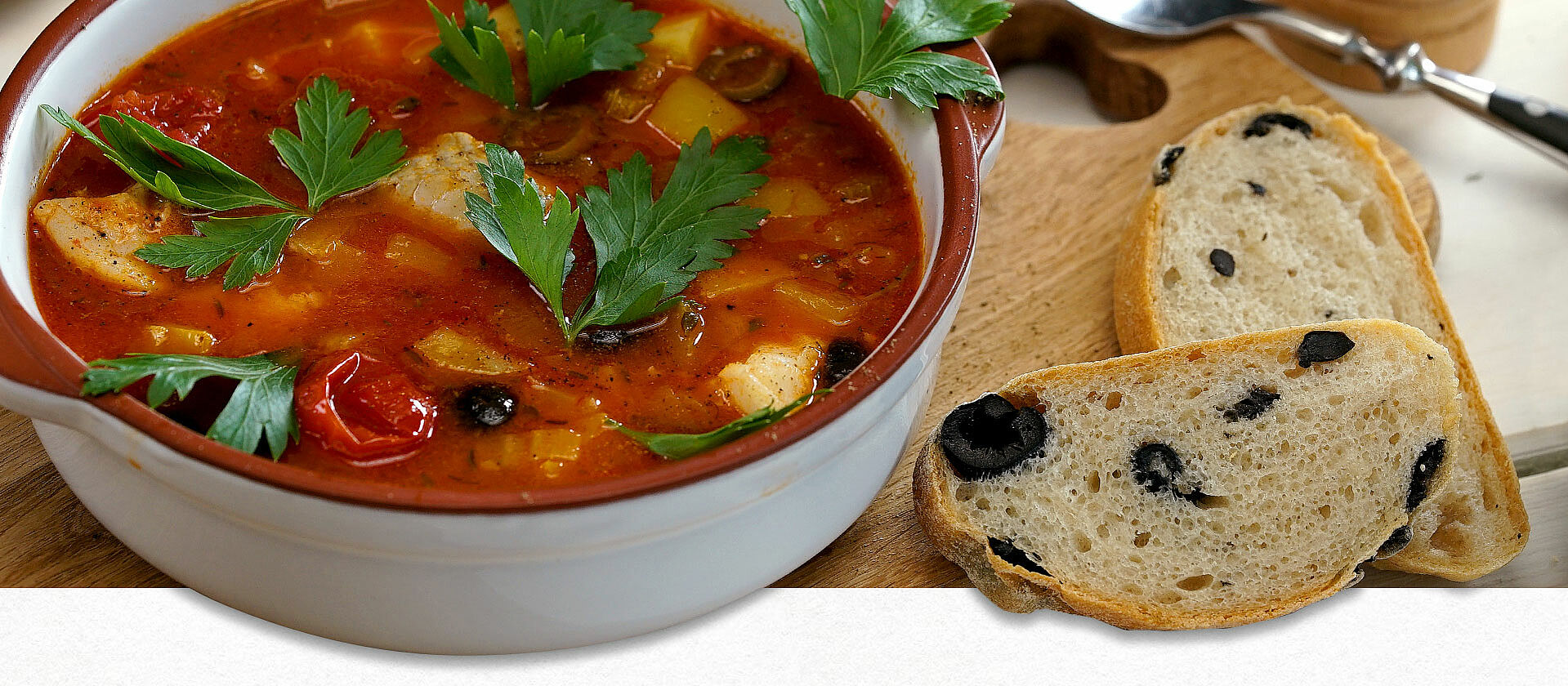 Eine Schüssel mit Tomaten-Fischsuppe, daneben zwei Scheiben Olivenbrot