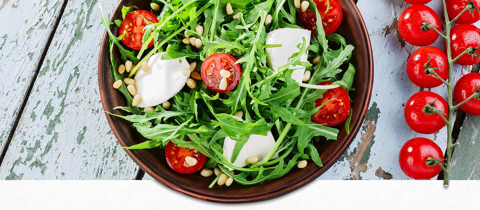 Rucola mit Tomate und Mozzarella in einer Schale auf Holztisch