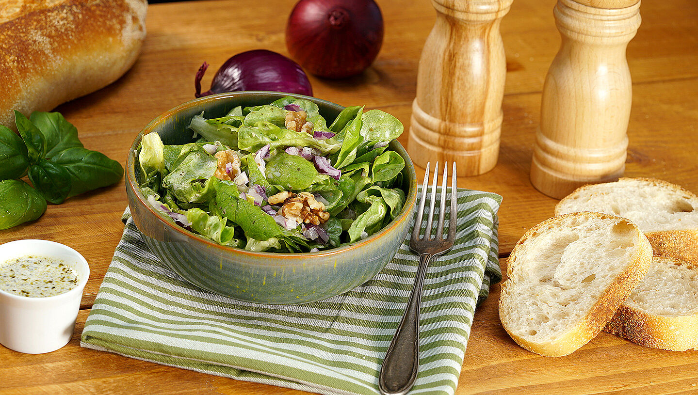 Eine Schüssel mit grünem Salat, Zwiebeln, Walnüssen und Dressing