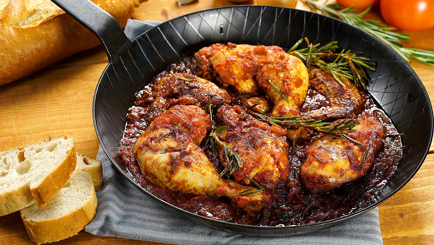 Eine Pfanne mit Hähnchenkeulen in Tomaten-Rotwein-Sauce