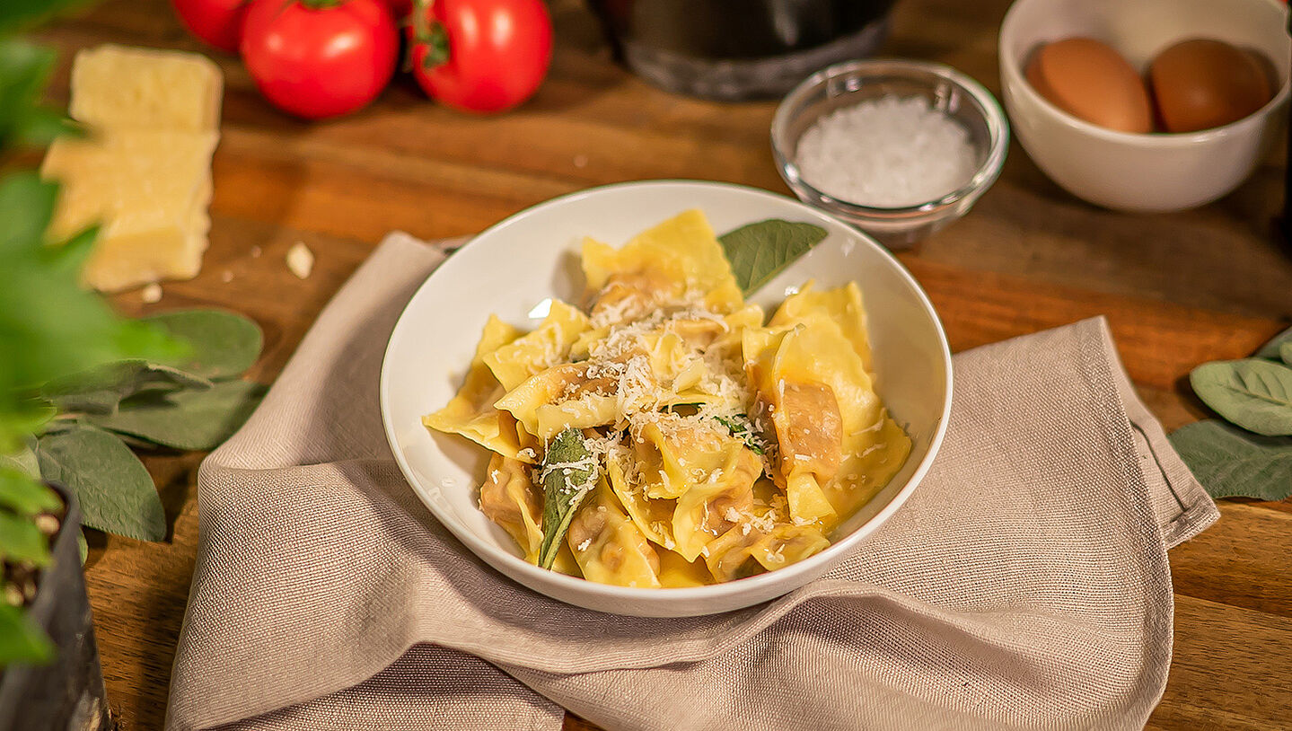 In einer weißen Schüssel sind italienische Agnolotti zu sehen. Die Schüssel steht auf einem beigen Küchentuch. 