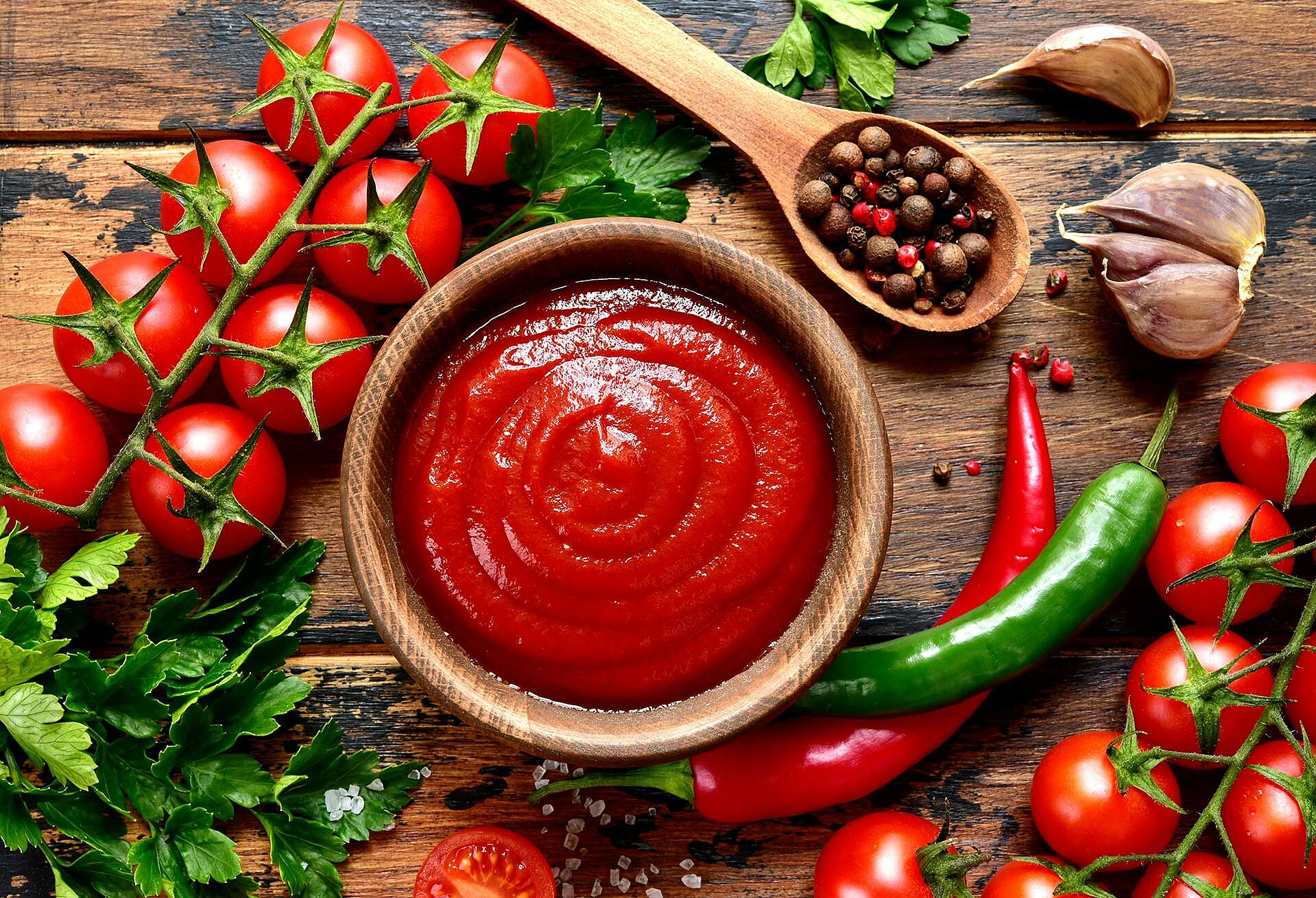 Passierte Tomaten in einer Holzschüssel. Frische Tomaten, Basilikum, Pfefferkörner liegen daneben.