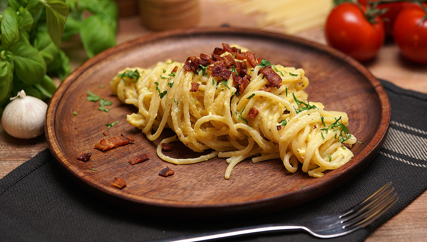 Original Spaghetti Carbonara auf einem Holzteller mit Pancetta-Würfeln