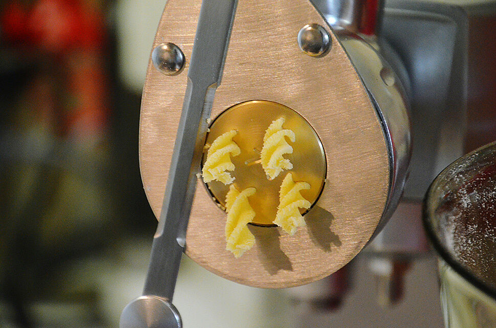 Aus einer Nudelmaschine kommen Spirelli-Pasta