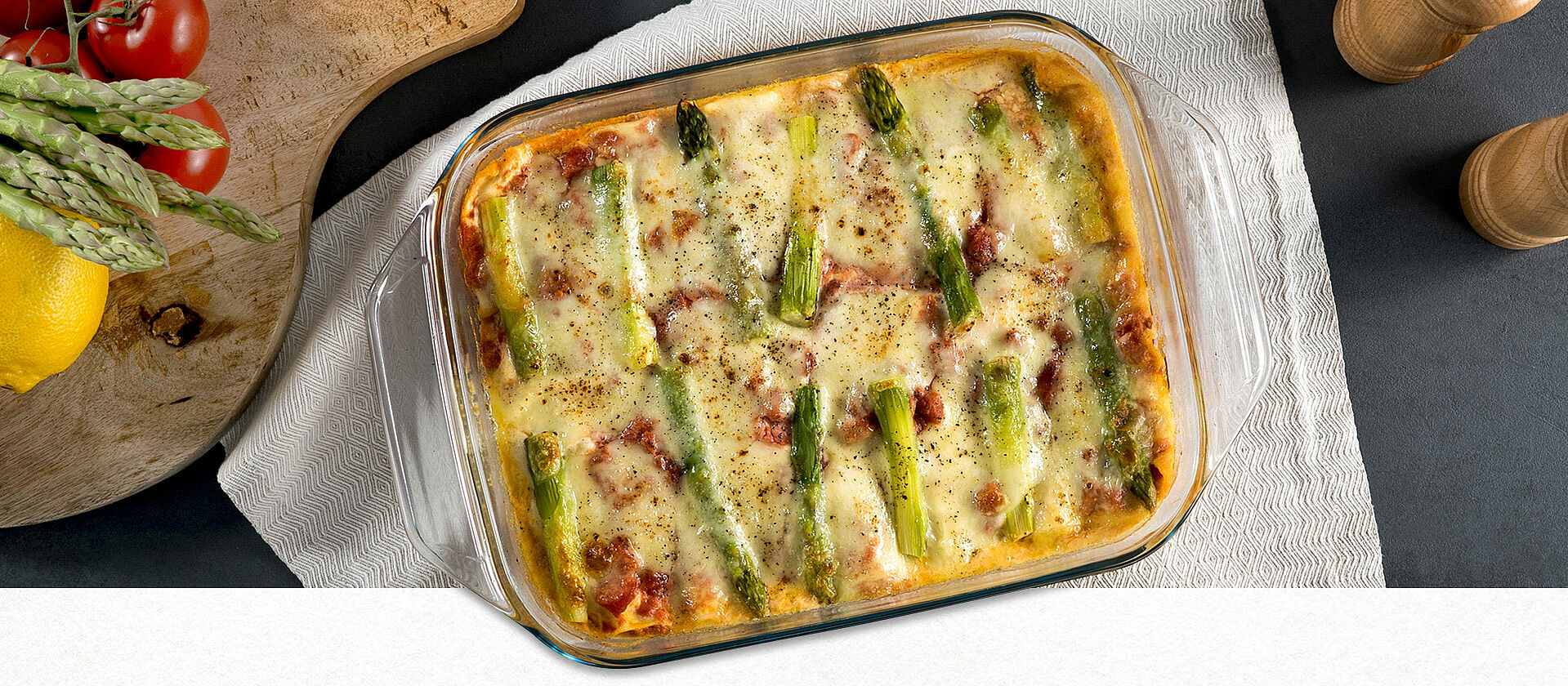 Lasagne mit grünem Spargel in einer durchsichtigen Auflaufform auf einem weißen Geschirrtuch. 