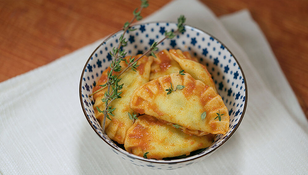 Ravioli mit Tomatensauce in einer Schüssel angerichtet und mit Kräutern garniert