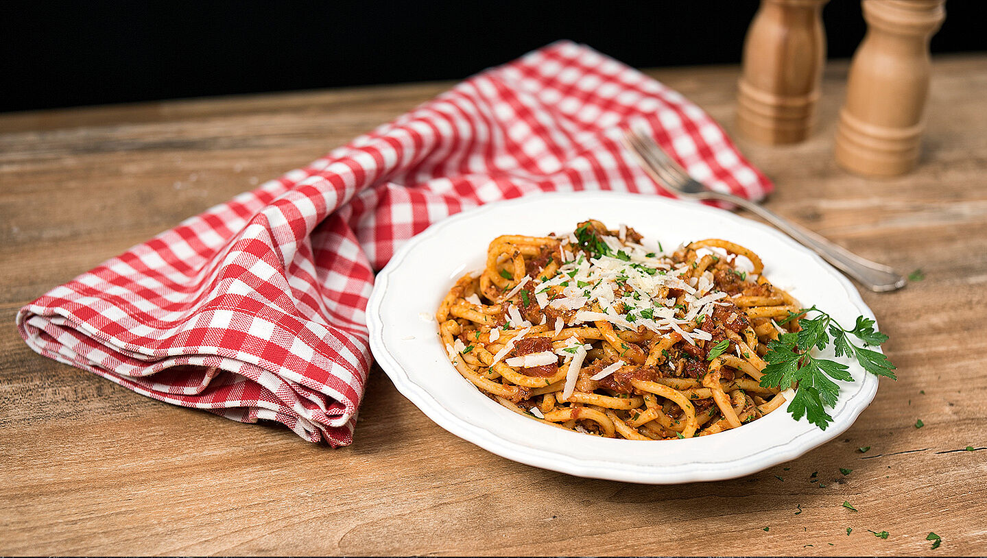 Bucatini-Nudeln mit Tomatensauce auf einem weißen Teller angerichtet. 