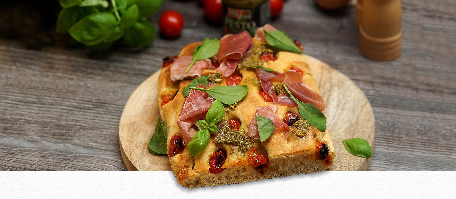 Focaccia mit grünem Pesto und Parma Schinken liegt auf einem Holzbrett