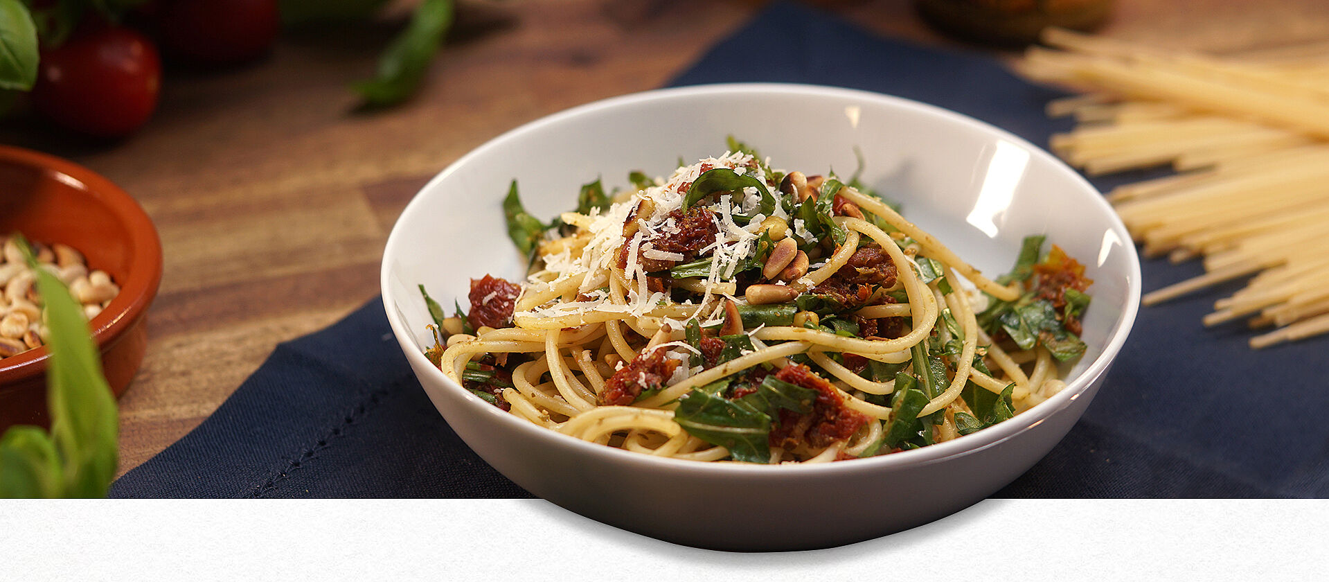 Eine Schüssel mit italienischem Spaghettisalat bestehend aus Rucola, getrockneten Tomaten, Spaghetti und Parmesan.