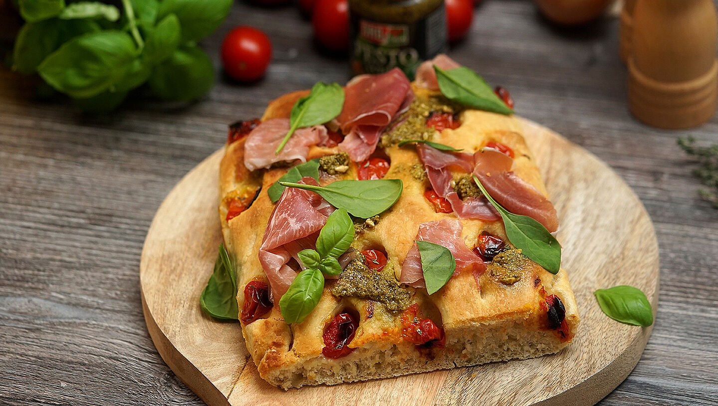 Focaccia mit grünem Pesto und Parma Schinken liegt auf einem Holzbrett