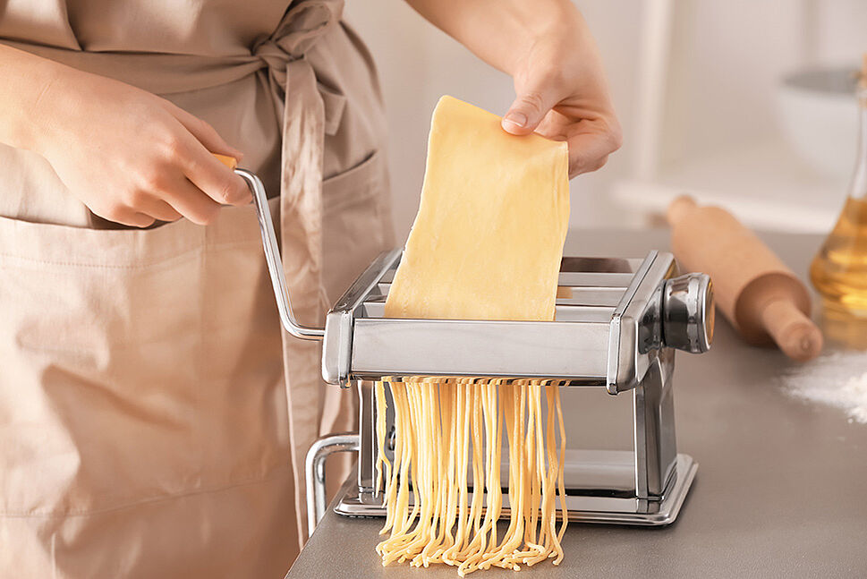 Eine Nudelmaschine durch die eine Pasta-Platte zu Bandnudeln verarbeitet wird