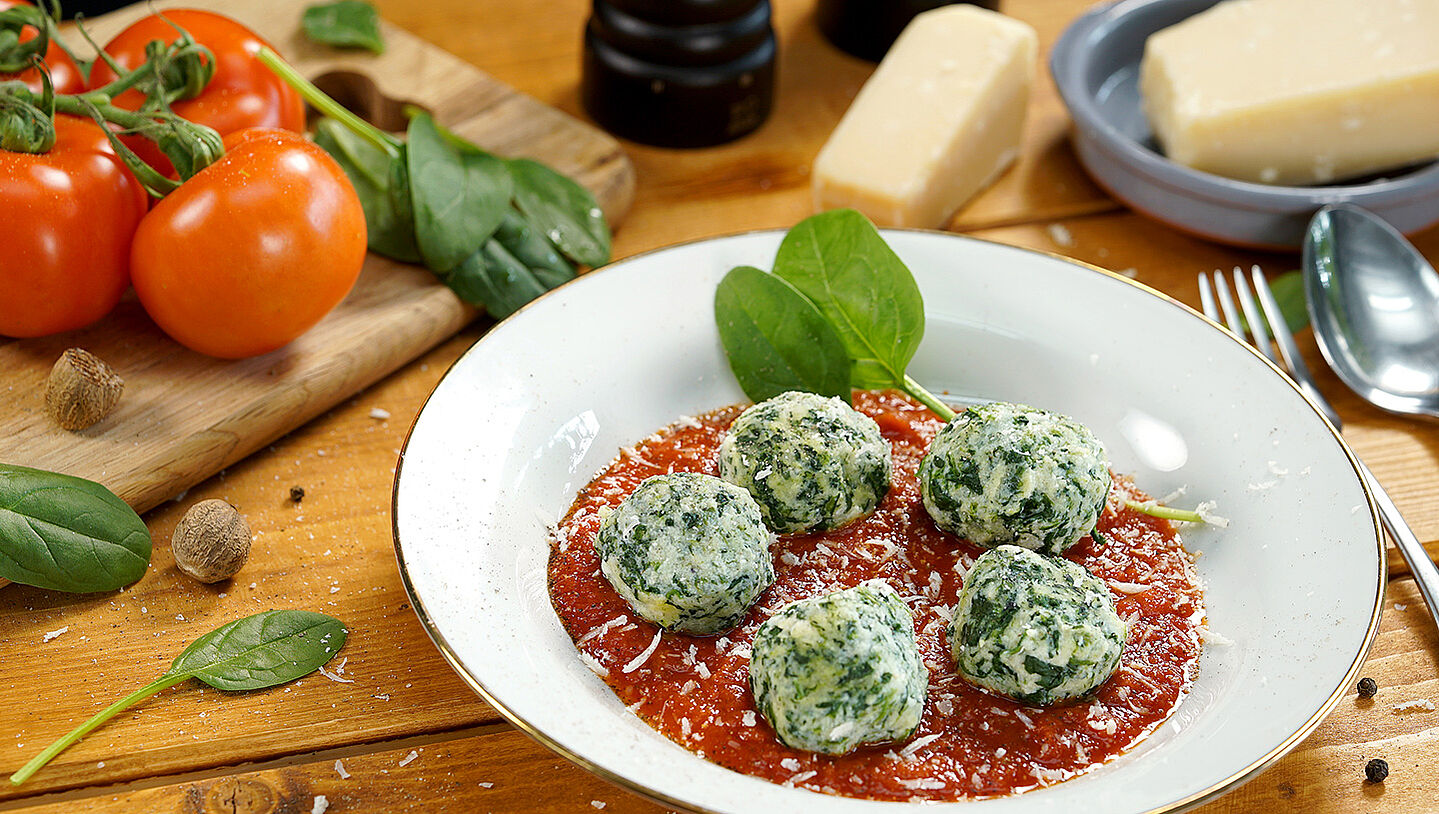 Ein weißer Teller mit Malfatti auf Tomatensauce