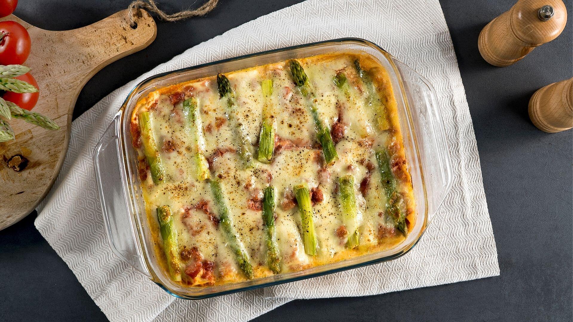 Lasagne mit grünem Spargel in einer durchsichtigen Auflaufform auf einem weißen Geschirrtuch. 