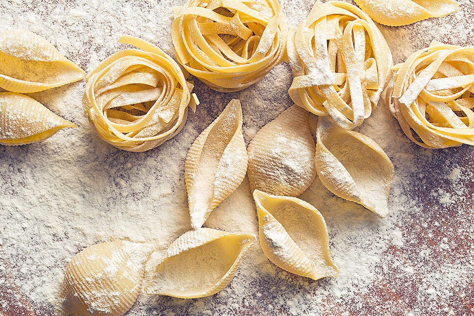 Tagliatelle und Muschelnudeln liegen auf einer Holzplatte