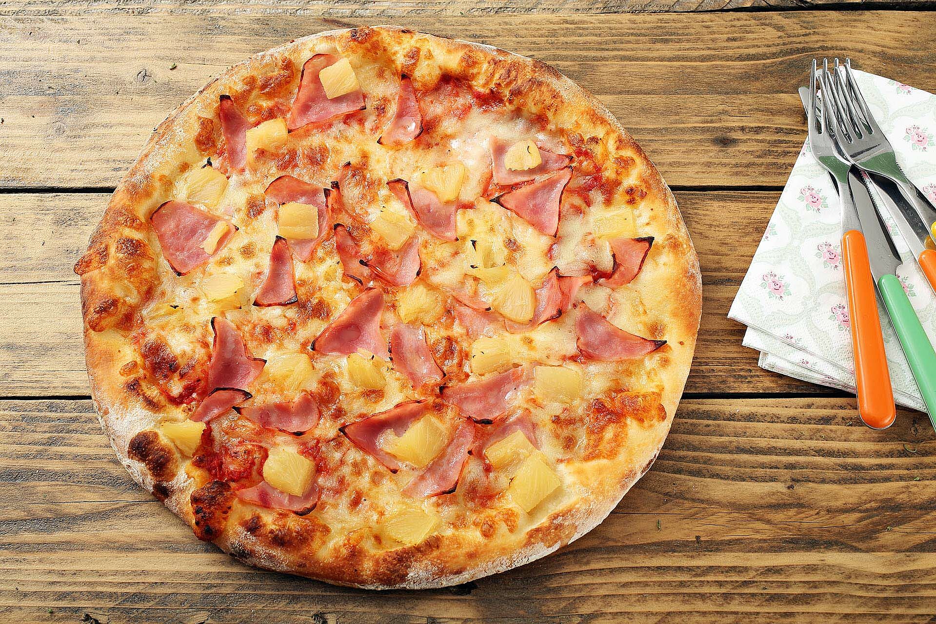 Pizza Hawaii mit Ananas und Schinken auf einem Tisch