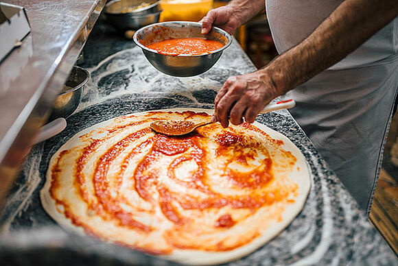 Tomatensauce wird auf Pizza verteilt