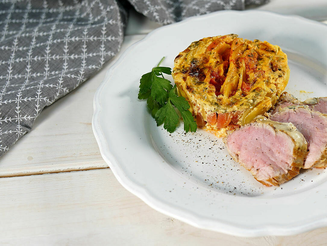 Ein Teller mit gratiniertem Schweinefilet und Tomaten-Kartoffel-Gratin