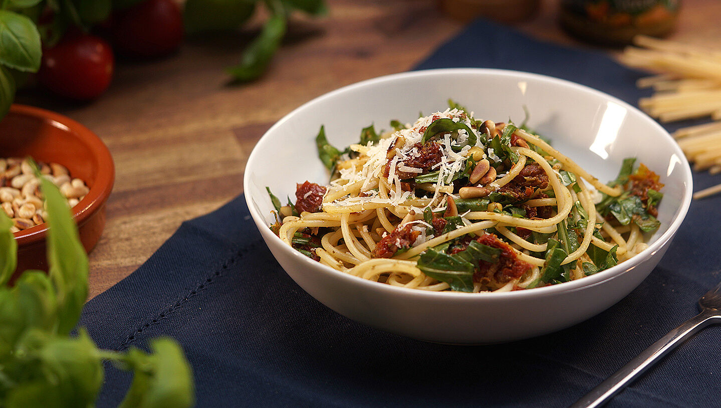 Eine Schüssel mit italienischem Spaghettisalat bestehend aus Rucola, getrockneten Tomaten, Spaghetti und Parmesan.