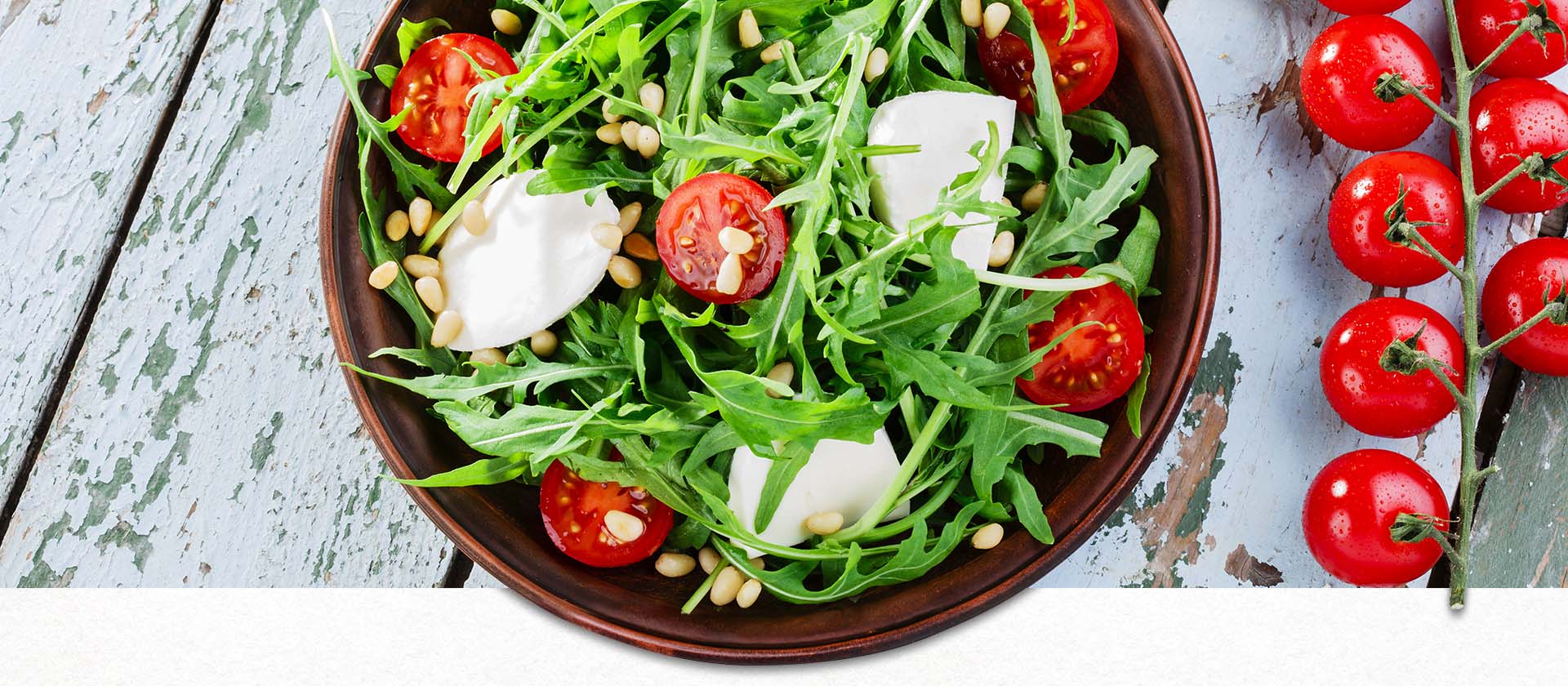 Rucola mit Tomate und Mozzarella in einer Schale auf Holztisch