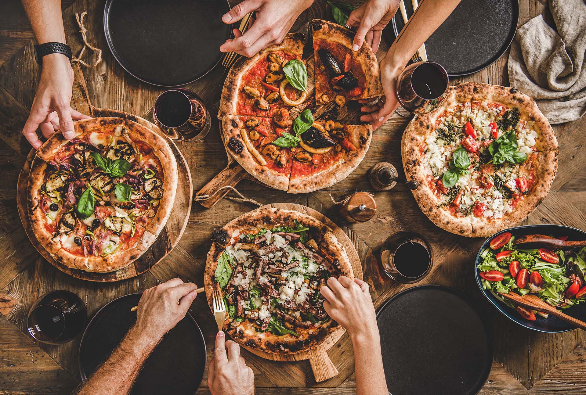 Freunde essen zusammen Pizza, verschiedene Pizzen auf einem Tisch