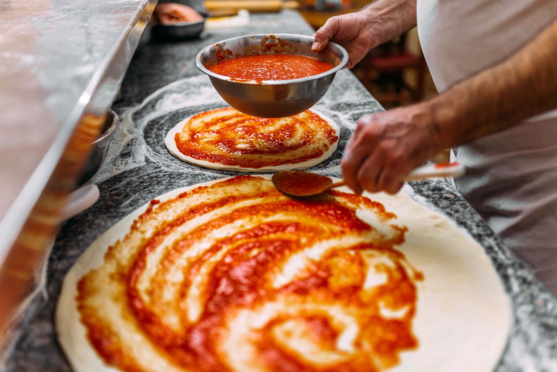 Pizzateig wird mit Tomatensauce bestrichen