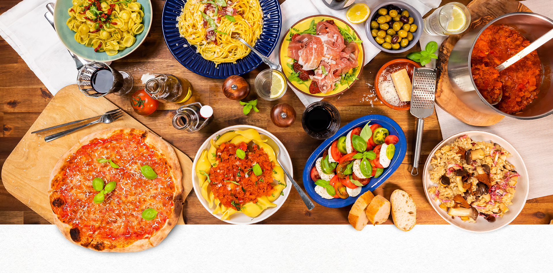 Auf einem Tisch steht eine bunte Mischung italienischer Gerichte. Pizza, Pasta, Tomate-Mozzarella-Salat und ORO di Parma Produkte. 