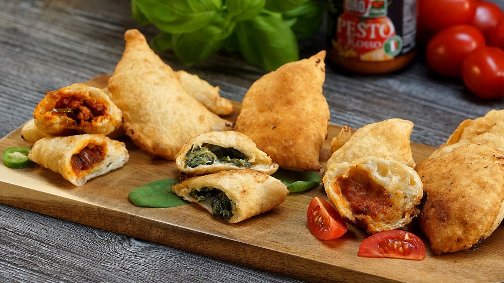 Auf einem Holzbrett liegen Panzerotti (italienische Teigtaschen) mit drei verschiedenen Füllungen