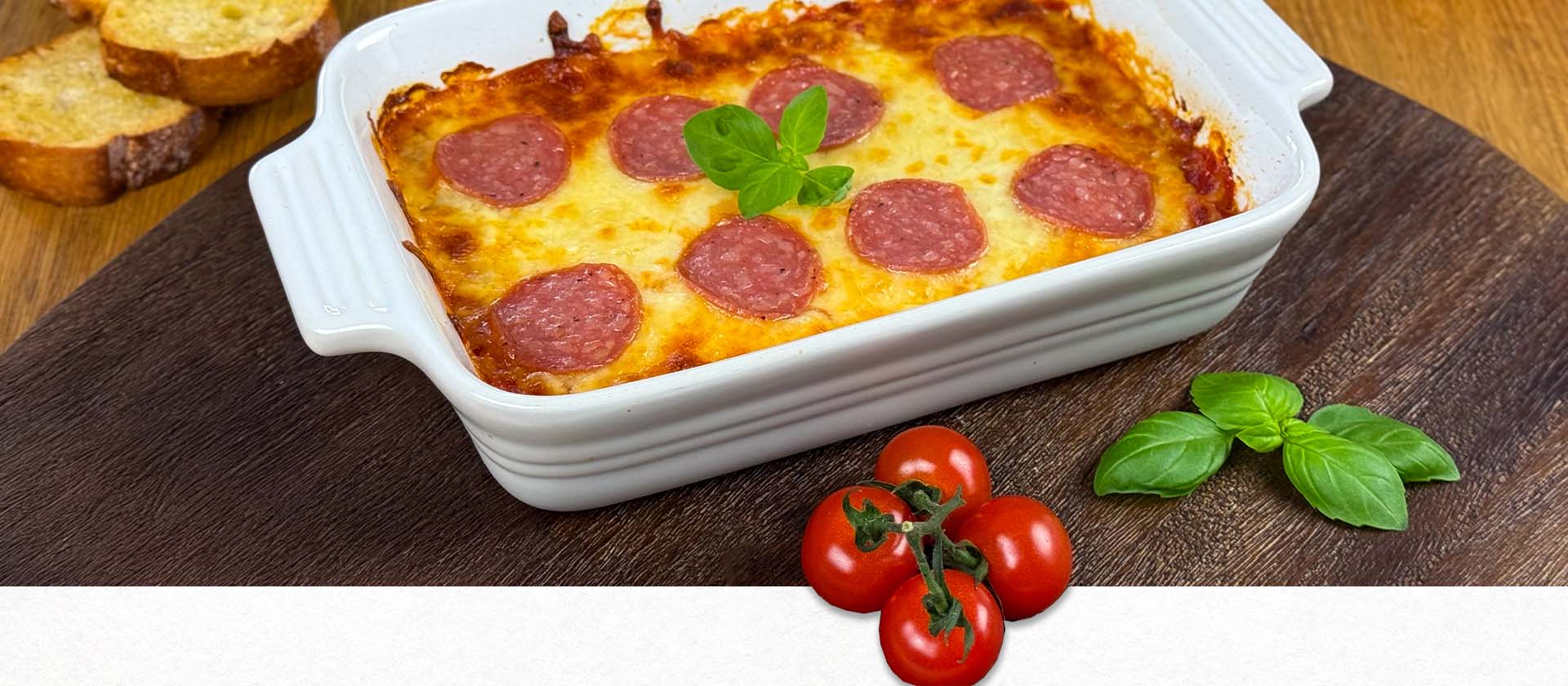 Pizzadip in Auflaufform mit Basilikum auf Holzbrett, dazu geröstetes Ciabatta.