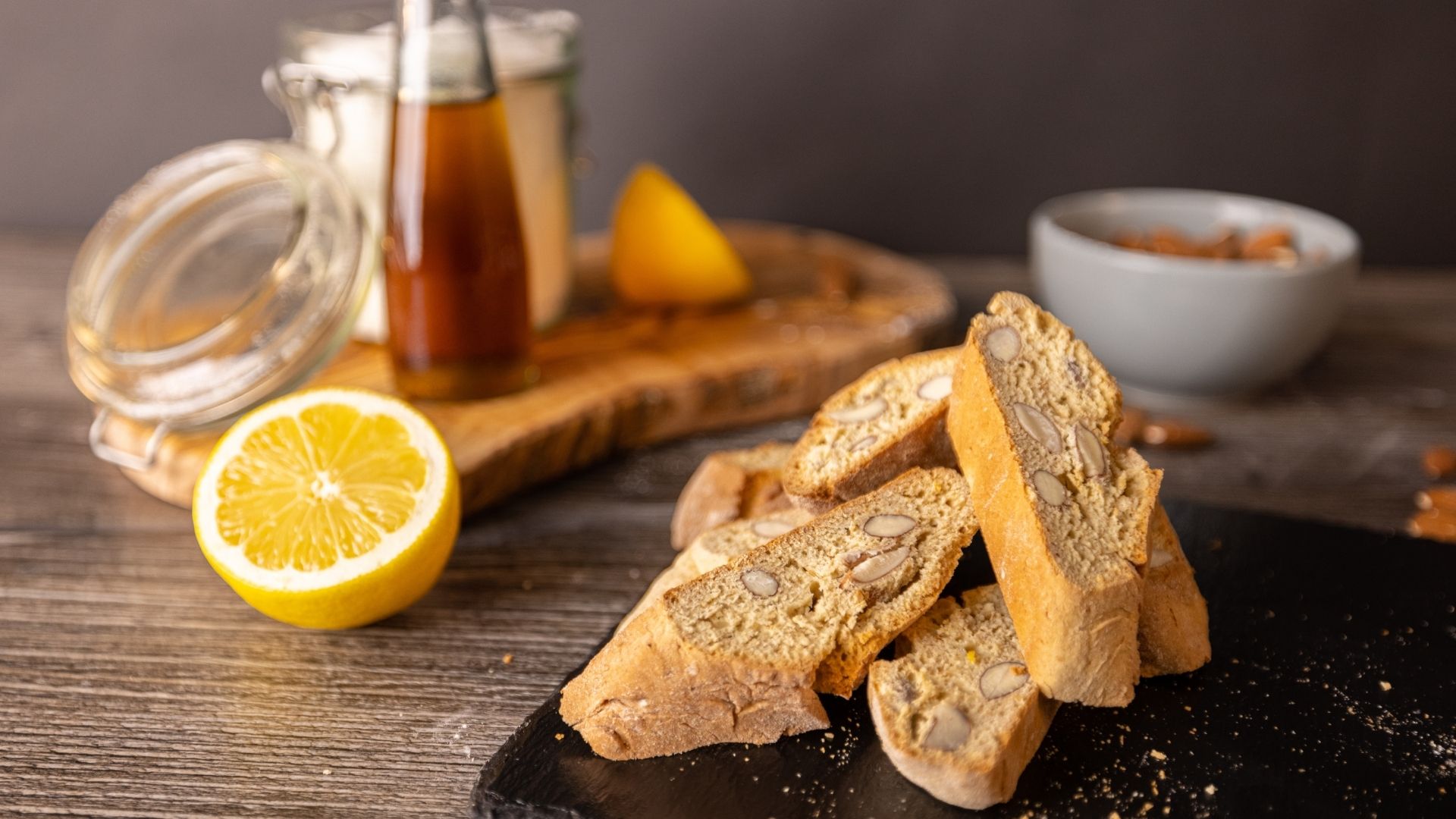 Auf einer Schieferplatte liegen 4 italienische Cantuccini. Im Hintergrund eine Tasse Kaffee.