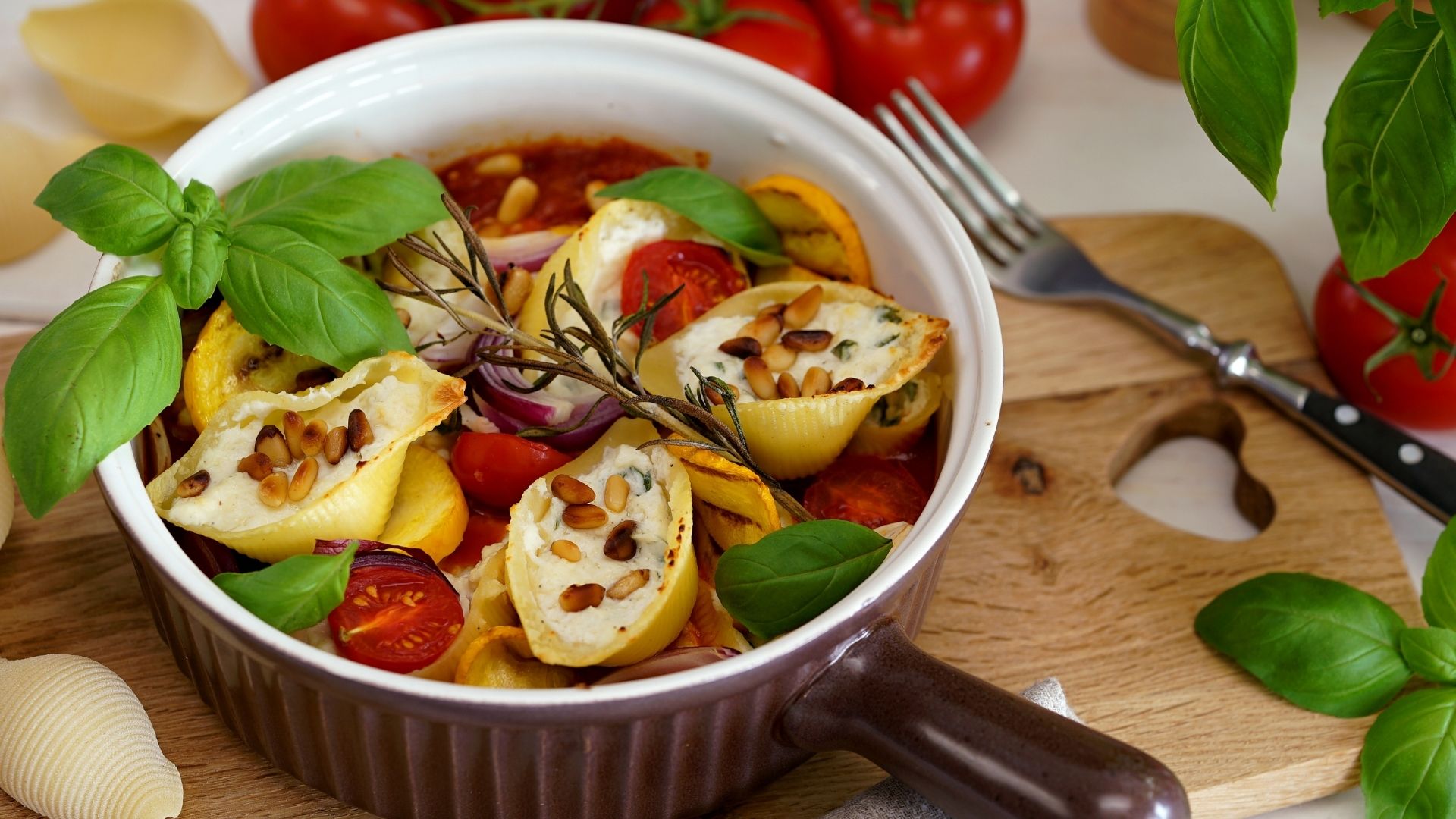 Eine runde Auflaufform gefüllt mit Muschelnudeln, mit Basilikumblättern garniert