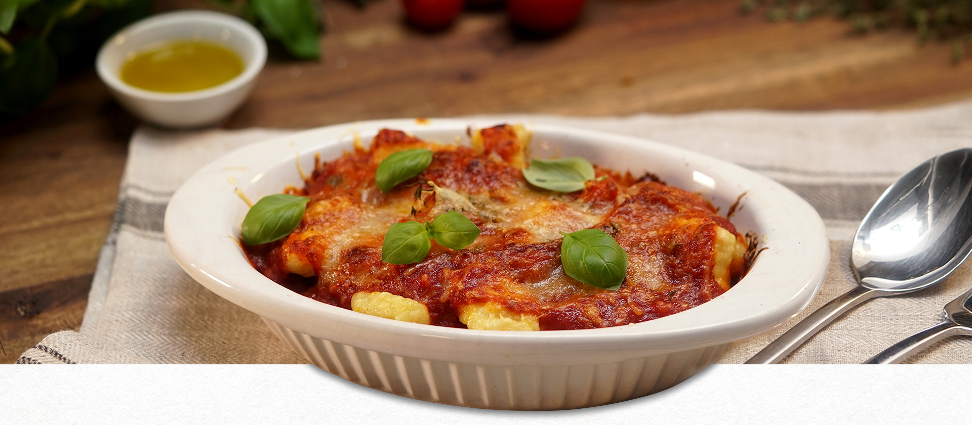 Mit Tomatensauce und Mozzarella überbackene Gnocchi in einer weißen Auflaufform mit Basilikum garniert